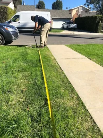 Plumber measuring sewer line with yellow tape along residential driveway