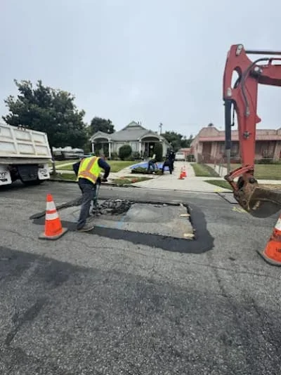 Excavator and crew performing sewer line repair on residential street with traffic control cones