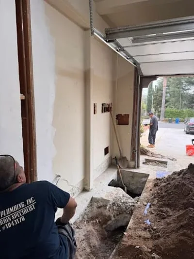 Plumbing crew installing foundation lines with excavated trench and new drywall opening
